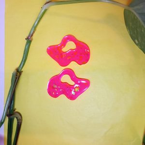 Par de pendientes de resina epoxi con forma orgánica irregular en color rosa fucsia translúcido, con pequeños destellos dorados en su interior.