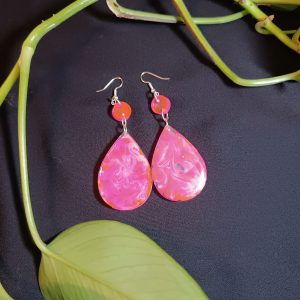 Par de pendientes de resina epoxi con una pieza circular y otra en forma de lágrima. Presentan un diseño de mármol con tonos rosados y naranjas.