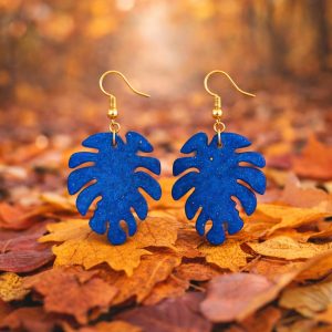 Pendientes Monstera Azul con forma de hoja sobre fondo otoñal.